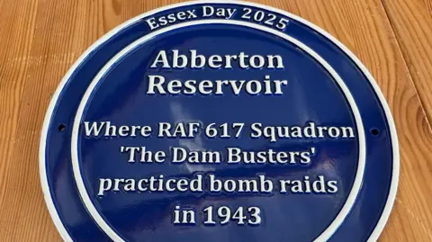 Nicola Laver/Essex & Suffolk Water A circular blue plaque that has white font on it, reading: "Essex Day 2025. Abberton Reservoir. Where RAF 617 Squadron 'The Dam Busters' practiced bomb raids in 1943."