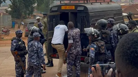 Bobi Wine/X Armed men in uniform lead a man into the back of a car