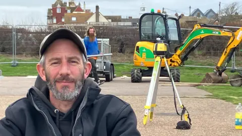 Guy Campbell/BBC Carl Hurr at Southwold's skatepark with digger and the town's lighthouse in the background