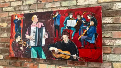 A photo of a painting by Paul Branson of a group of musicians hung on a brick wall