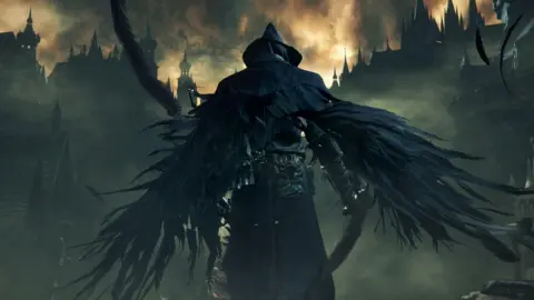 Sony/FromSoftware A hooded figure stands facing a Bloodborne scene, which is a fiery and dark landscape with turrets and buildings on the horizon. The figure has their back facing the picture, and is wearing dark feathered wings and a dark hat.