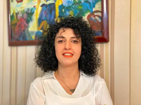 Reuters A woman with curly black hair dressed in a white collared shirt and red lipstick, smiles to the camera. 