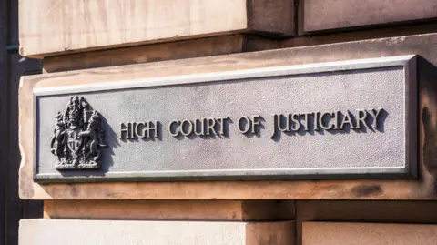 Getty Images A metal sign on a sandstone block exterior wall that has a crest and the words: "High Court of Justiciary".