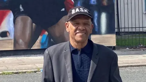 Howard Gayle stood by the mural, wearing a cap and smiling.