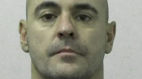 Mugshot of a bald man with slight stubble.