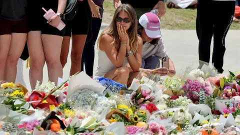 Getty Images Mourners gather by floral tributes at the Bondi Pavillion in memory of the victims of a shooting at Bondi Beach, in Sydney