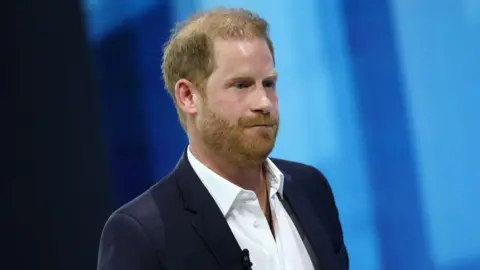 Getty Images File photo of Prince Harry on a blue background, wearing a white open-neck shirt and a dark blazer.