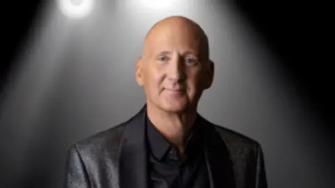 Family handout A headshot of Ian Gore, he has a shaved head and wears a glittery black jacket over a black shirt