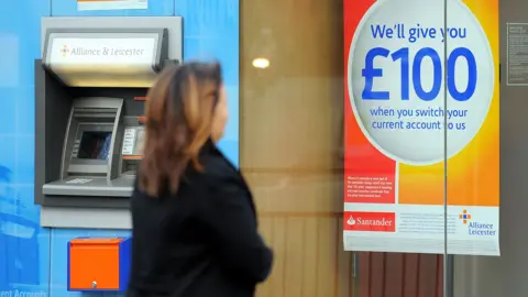 Woman wearing a dark coat looks at a sign that reads: Sort out your finances. We'll give you £100 when you switch your current account to us.