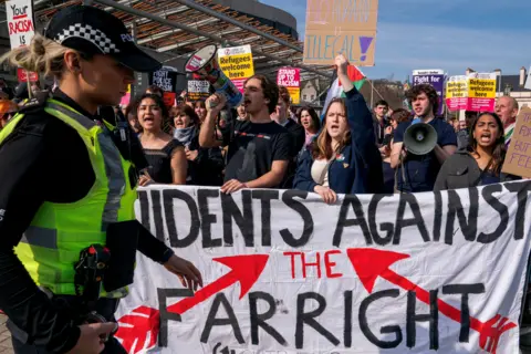 PA Media A crowd of protestors standing behind a white banner which reads: Students Against The Far Right". A police officer can be seen in the left hand side of the shot, which has been taken outside the Scottish parliament building.
