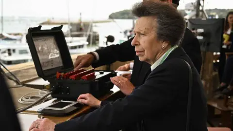 Cowes Week Martin Allen The Princess Royal with a dark top and green and white striped collar watches race operations from a control room overlooking the harbour.