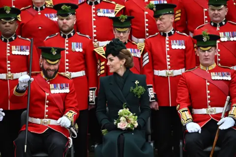 PA Media Princess of Wales sitting down holding a bouquet of flowers, surrounded by at least ten members of the Irish Guards in red uniform.