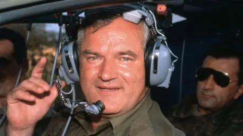 Gamma-Rapho via Getty Images Ratko Mladić is photographed wearing ear defenders in a military helicopter during the Bosnian War in 1994