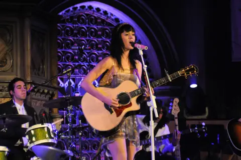 Getty Images Katy Perry playing an acoustic guitar in Union Chapel. A drummer and guitarist are sat playing behind her