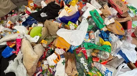 Victoria Gordon A huge pile of rubbish, which is made up of boxes, bin bags and food packets. It covers the screen.