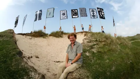 WOMAD Angus Watt sitting in front of a row of WOMAD flags
