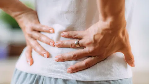 A person holding their back. They have a ring on their right hand.