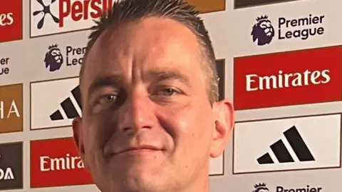 Family handout A man, with brown hair, smiling for camera. He is in front of a board full of adverts.