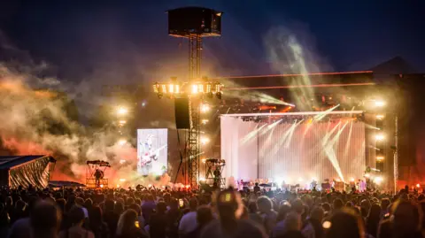 Getty Images A large stage with lights and smoke and a large crowd