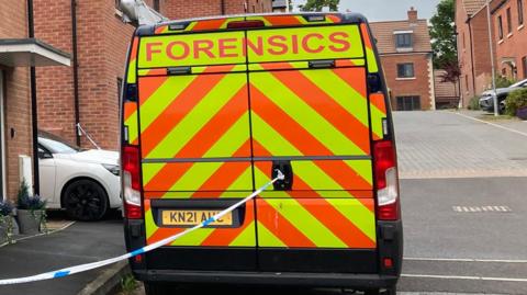 The back of a florescent yellow and orange police forensics vehicle parked outside a red brick house on Strawberry Fields road in Easterton. There is also police tape visible which is cordoning off a house. 