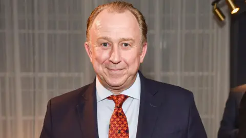 Nigel Blow wearing a blue suit and orange tie at the opening of the Turnbull and Asser store in Mayfair, 2015