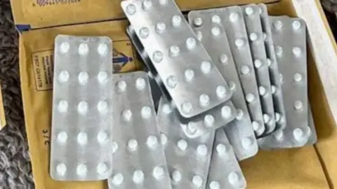 Several white pills in a silver blister pack are placed on top of a brown manila envelope.