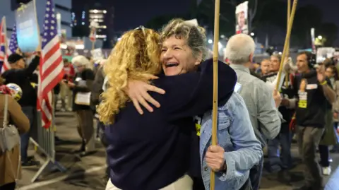 EPA Two women hug in the middle of crowded protest at night. The woman facing the camera is smiling while holding a placard.