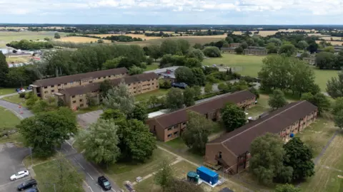 PA Media Aerial shot of the housing blocks at an airbase. Four rectangular accommodation blocks can be seen, surrounded by grass, trees and roads. There are agricultural fields in the background.