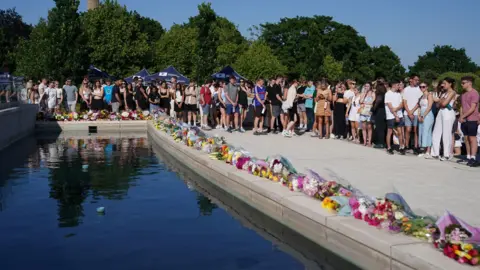 PA Media Dozens of students alongside a row of flowers