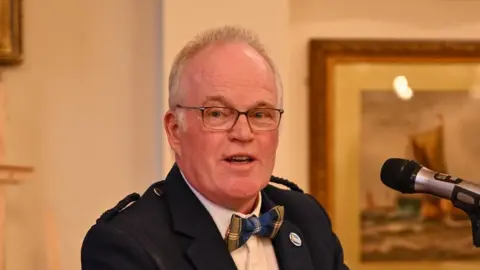Supplied A head and shoulders image of a man wearing glasses, black blazer and a bow tie.