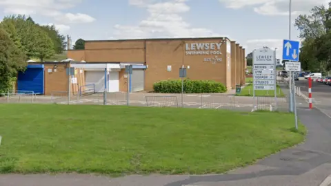 The outside of Lewsey Swimming Pool, with a sign advertising sports available at Lewsey Sports Park