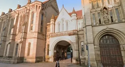 Google Maps There is an archway in the middle of the Gothic-style building with a sign above it which reads: University of Manchester 