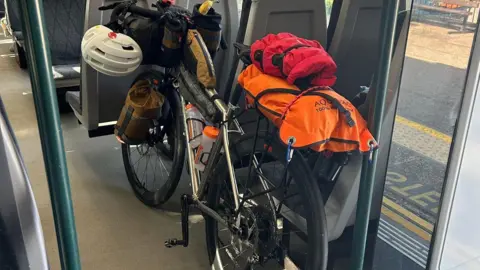 Norman Brown A bike with bags is parked inside a train carriage between seats.