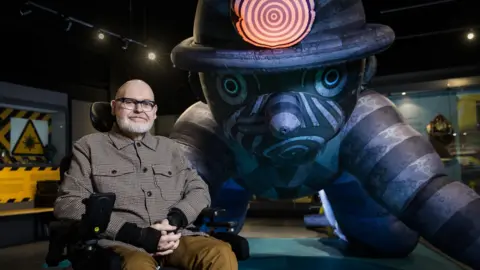 National Coal Mining Museum A man sits in a wheelchair next to a huge sculpture depicting a miner on his hands and knees.
