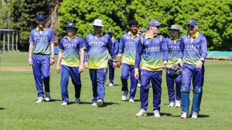 ETDC Digital Media A group of Oxford cricketers dressed in blue and yellow kit walk off the field whilst chatting to one another.