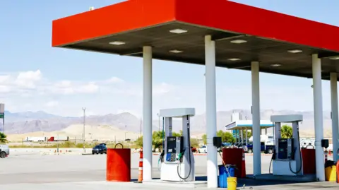 A petrol station with a bright red awning sits in the foreground, with a long mountain range in the background.