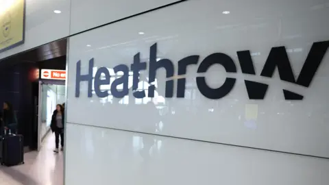 NEIL HALL/EPA-EFE/REX/Shutterstock Sign reading Heathrow inside airport terminal. There is an unidentified woman, who is out of focus, walking towards the sign in the background.