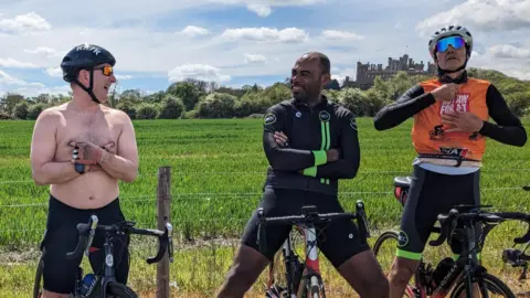 Members of cycling clubs across The Vale of Belvoir pictured astride their bikes. One is naked from the chest up but has his arms folded. Two more cyclists are sat on their bikes fully clothed. All three are laughing together.