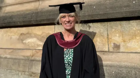 A woman wears a gradation cap and gown to collect her degree. 