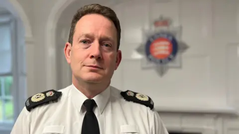 Stuart Woodward/BBC Ben-Julian Harrington pictured wearing a police uniform standing in police headquarters