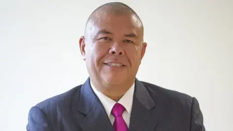 Professor Sir Jonathan Van-Tam, the chair of the Lincolnshire Football Association. He is wearing a blue pinstripe suit and a purple tie