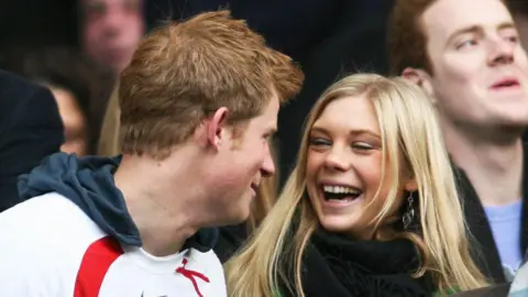 CHRIS RATCLIFFE/AFP via Getty Images Prince Harry in an England rugby top and Chelsy Davy in a bright green coat and black scarf laugh before the game between South Africa and England at the Investec Challenge international rugby match at Twickenham