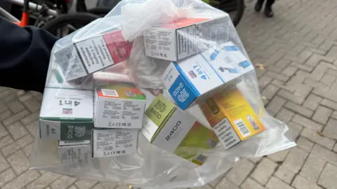 A clear bag containing small cardboard boxes with vapes inside