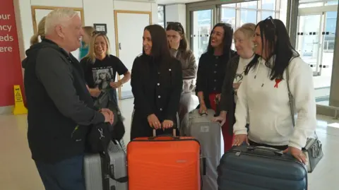 Ian Western with his friends and family at Aberdeen Airport. They are standing in a group holding suitcases.