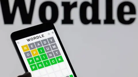 A hand holding a phone showing the Wordle app