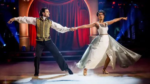 Julian Caillon and Balvinder Sopal who is wearing in a white flowing dress dance a Viennese Waltz in the studio on Strictly Come Dancing
