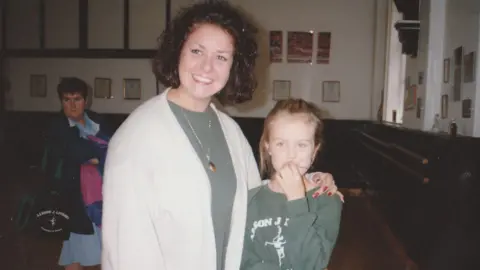 Claire Booth Claire Booth is pictured as a child in a dance studio wearing a green jumper next to Alyson Livesey who is has shoulder length hair and is wearing a cream cardigan and green top and a gold necklace.