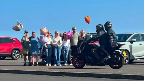 A biker rides past a group of people, a red balloon is flying in the background