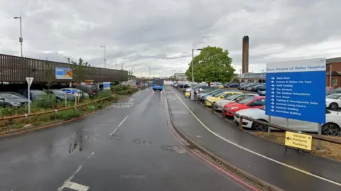 Google The entrance to a parking area at Grimsby's Diana, Princess of Wales Hospital, with direction signs, a small multi-storey car park and a bus travelling down the road.