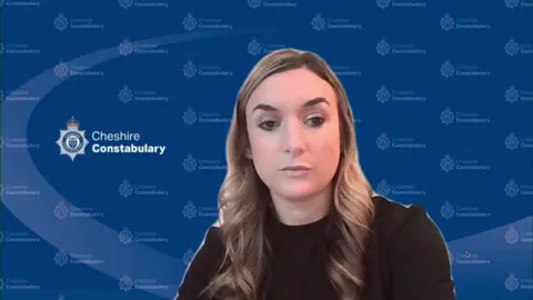 Ch Insp Amber Hodson, who has blonde wavy hair, looks into the camera with a serious expression. In the background is a blue screen displaying a Cheshire Police crest.